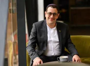 KAICIID Fellow Alex Goldberg smiles at camera as he sits with a cup of coffee